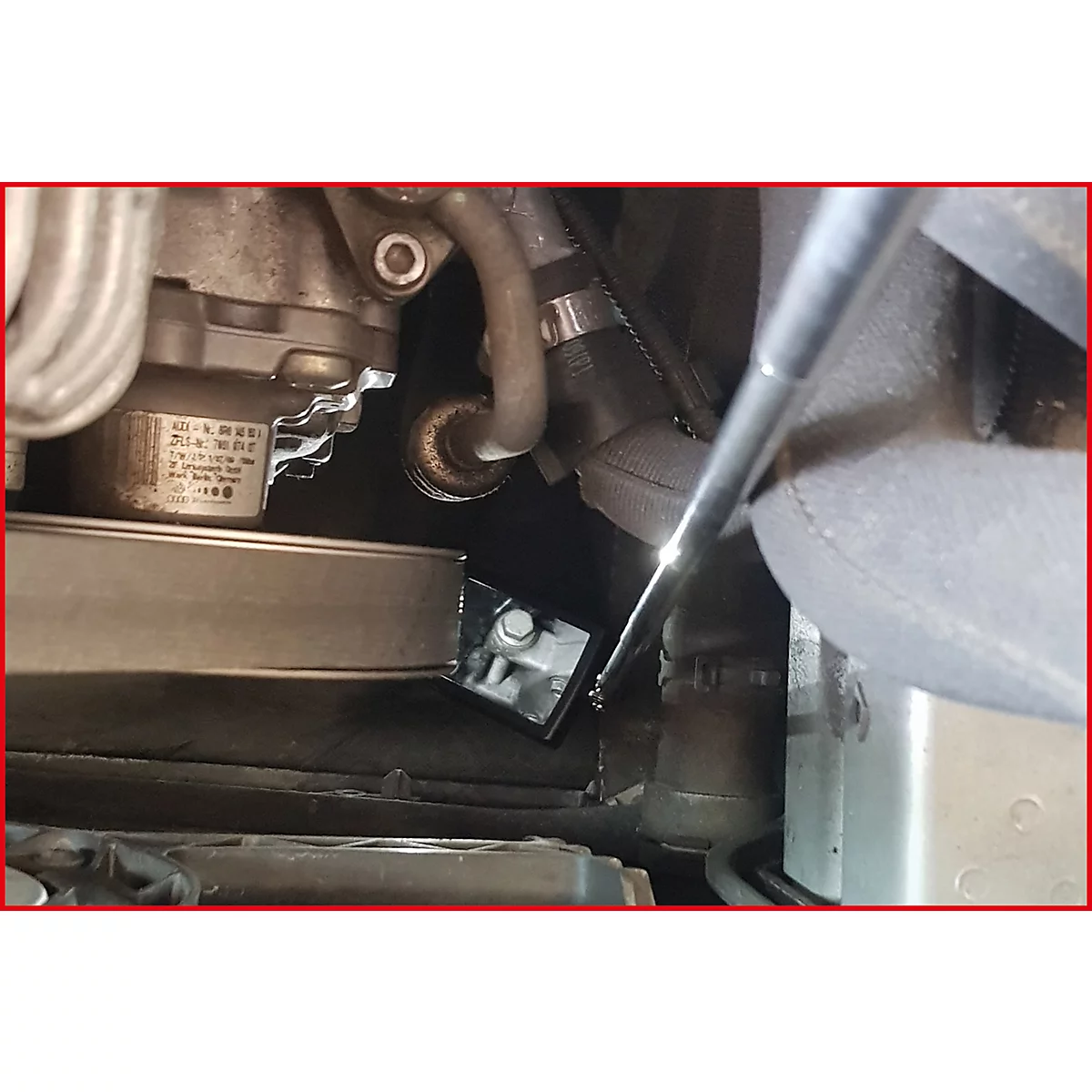 Nahaufnahme eines Motorraums mit verschiedenen Komponenten. Ein Werkzeug wird in das Bild gehalten.